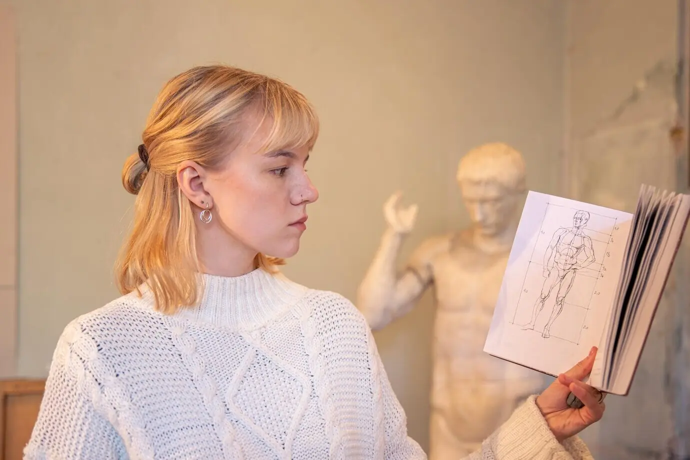 Mujer artista joven y atractiva que lee un libro de anatomía; concepto de aprendizaje.