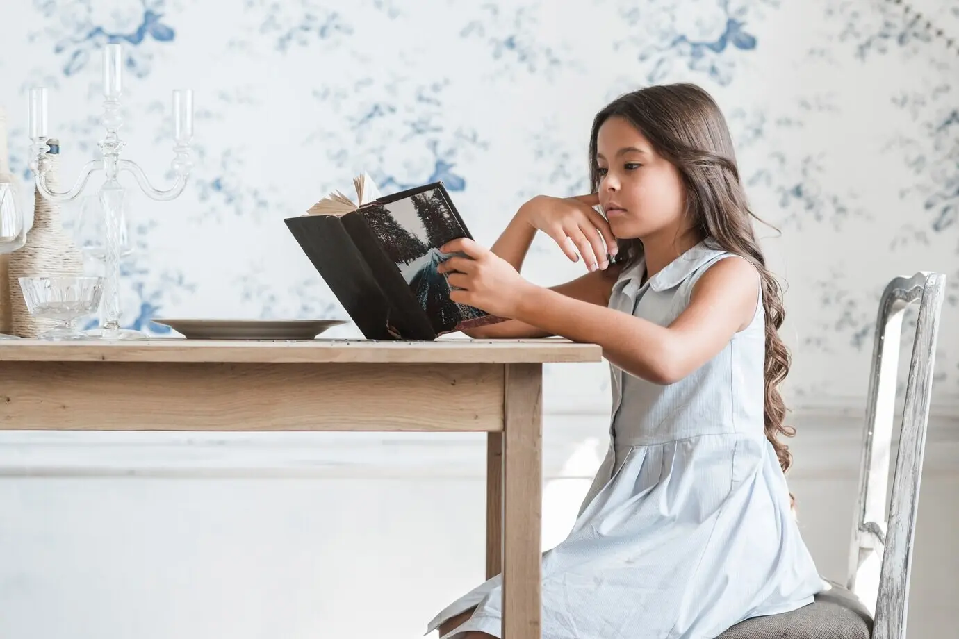 Vista de perfil de una chica leyendo un libro en una mesa de comedor.